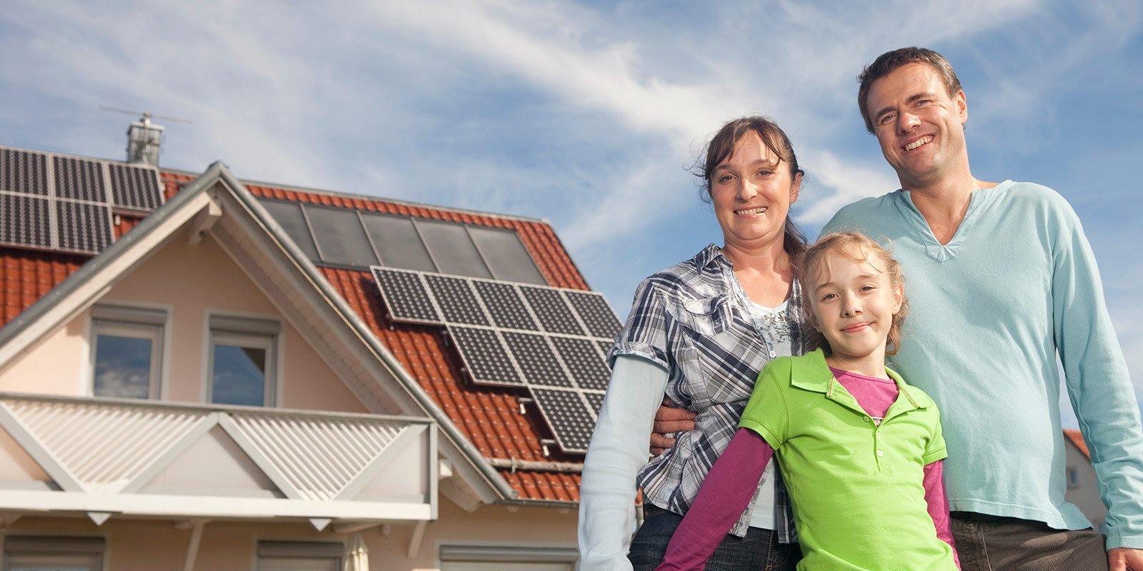 Eine kleine Familie, im Hintergrund ist ein Haus mit einer Photovoltaikanlage