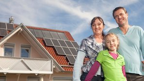 Eine kleine Familie, im Hintergrund ist ein Haus mit einer Photovoltaikanlage